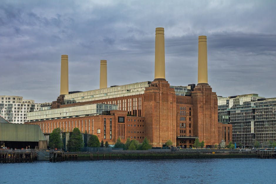 The image depicts the Battersea Power Station, a large industrial building with a brick facade featuring vertical and horizontal architectural details. Four tall, cream-colored chimneys extend upward 